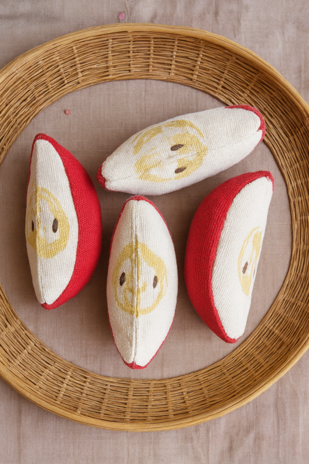 Four red and white plush toys shaped like slices of fruit with smiling faces on a woven basket.