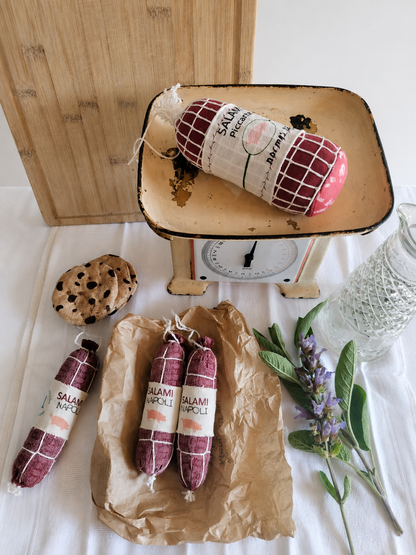 Handmade fabric Salami Napoli play food styled with a vintage kitchen scale, wooden cutting board, textile cookies, brown deli paper and fresh herbs in a rustic product setting