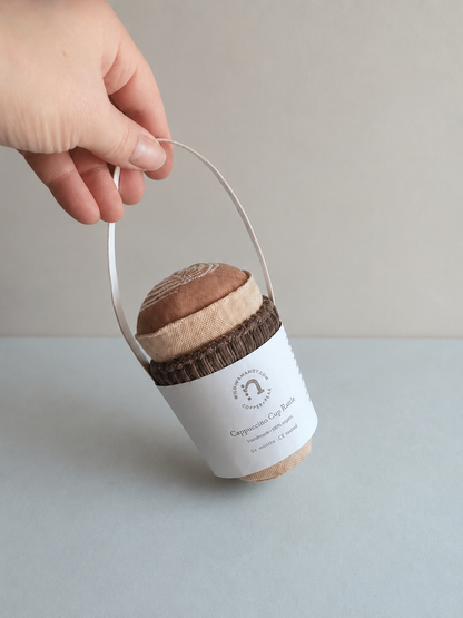 Hand holding handmade fabric play food cappuccino cup with label on neutral studio background