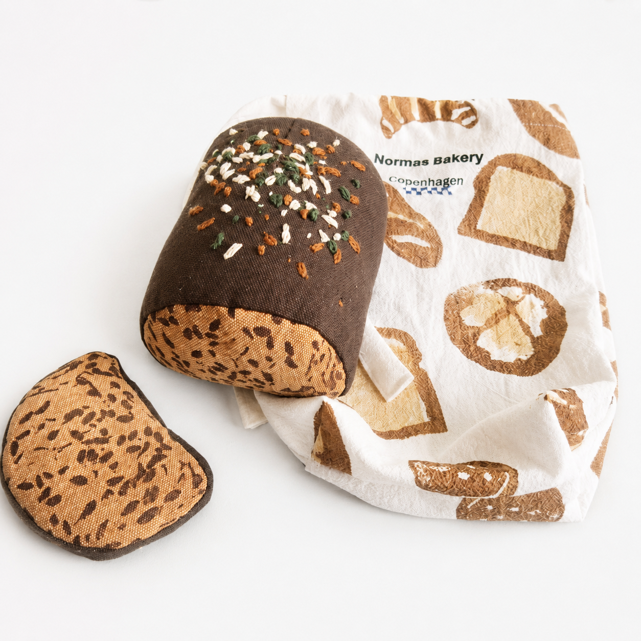 Handmade fabric rye bread loaf with one slice and a printed bakery cotton bag on a white studio background.