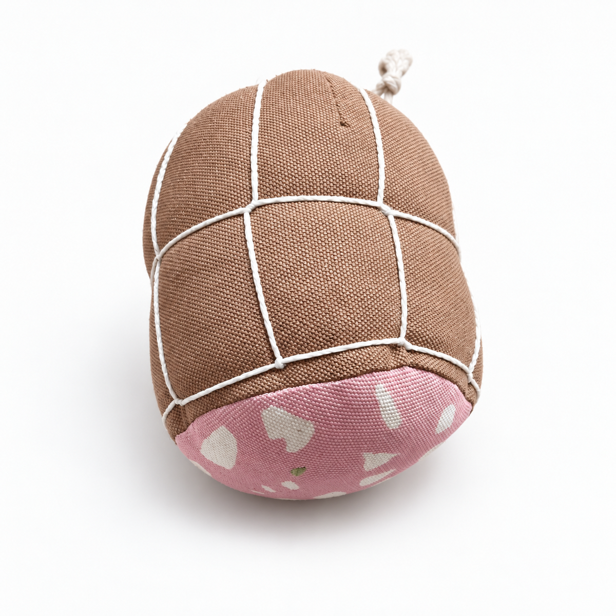 Front view of handmade fabric mortadella play food, featuring a pink patterned end, brown cotton canvas and white string netting on a soft off-white studio background.