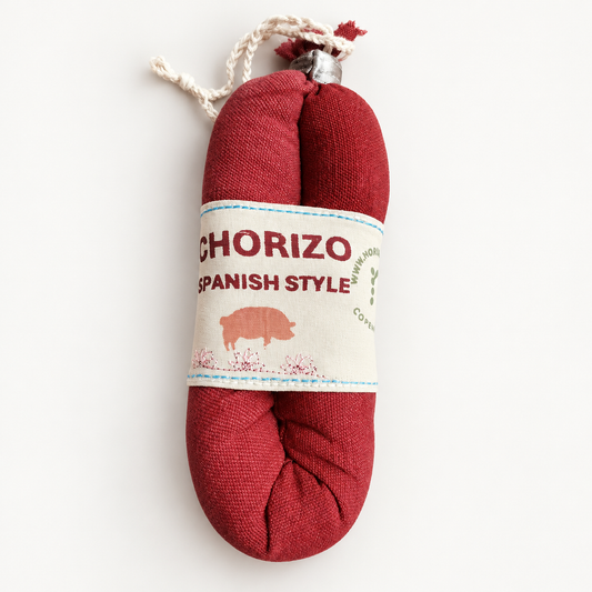 Handmade red fabric chorizo play food with a Spanish-style embroidered label and cotton string details, photographed on a soft white studio background.