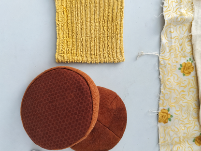 Handmade BMO play food components showing two brown sweatshirt fabric bun halves, a textured yellow cotton cheese slice and floral cotton fabric used in production.