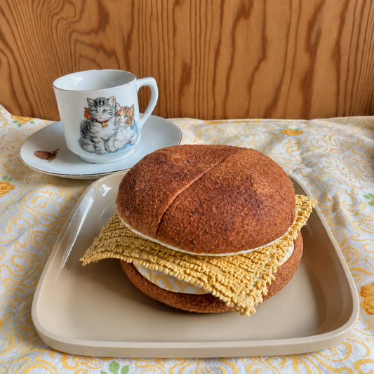 Handmade BMO (Danish bun with cheese) play food made from upcycled sweatshirt fabric and cotton, served on a beige plate beside a vintage kitten cup.
