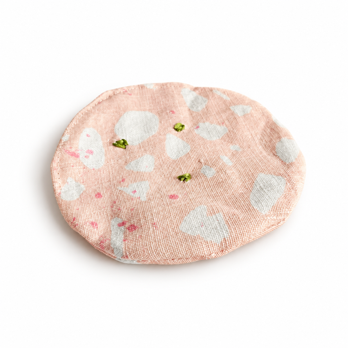 Handmade upcycled fabric mortadella slice in soft pink with white marbling and hand-embroidered green pistachios. Textile play food by normadot, made in Denmark.