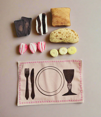Flat lay of a handmade fabric play food set including sandwich chocolate slices, chocolate spread toast, cinnamon toast, sourdough bread, strawberry slices, banana slices, and an embroidered placemat with a printed table setting.
Fladtlæggende visning af håndlavet legemad i stof med pålægschokolade, chokoladepålæg på toast, kaneltoast, surdejsbrød, jordbærskiver, bananskiver og en broderet dækkeserviet med trykt opdækning.