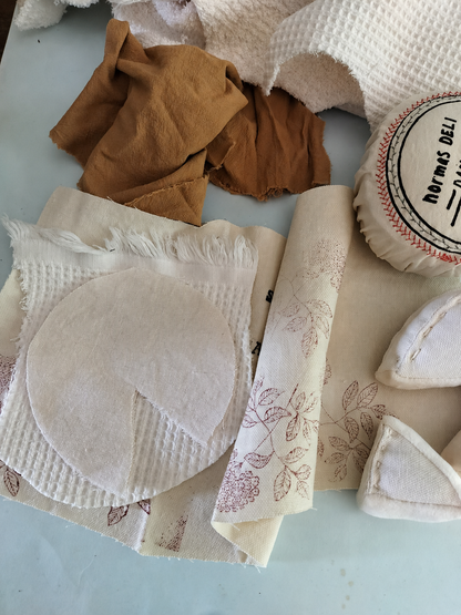 Handmade textile camembert play food in progress with cotton fabric pieces, printed cover, soft cheese wedges and fabric scraps for pretend play toy production.