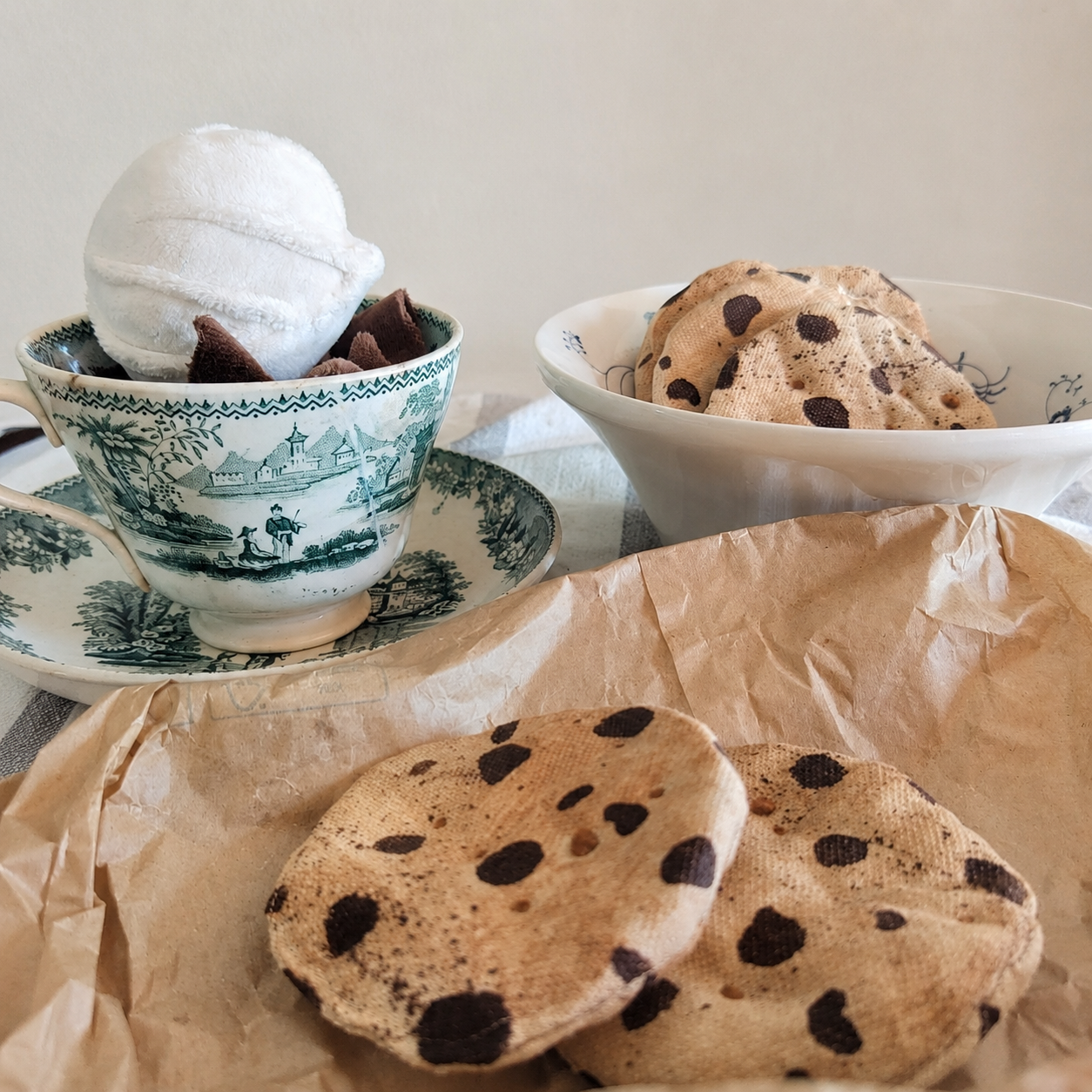 Handmade fabric chocolate chip cookies arranged for pretend tea party play with a vintage cup and bowl.