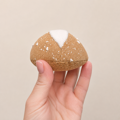 Hand holding a handmade fabric bread roll play food against a neutral background, handmade in Denmark by normadot