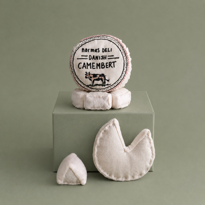 Handmade textile camembert cheese play food with removable printed cover, soft round cheese and small cheese wedge on brown paper for pretend play kitchens