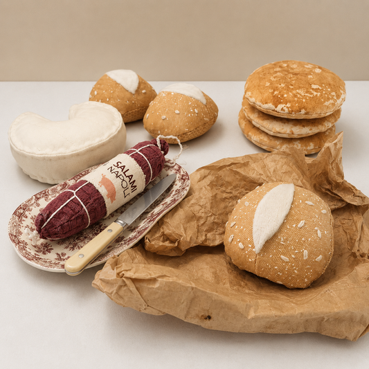 Handmade fabric bread rolls, pancakes, cheese and salami play food arranged in a bakery and deli scene.