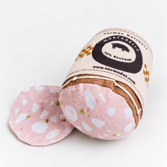 Handmade fabric mortadella with a separate pink slice, white printed details and green embroidery, wrapped in a Normas Butchery label.